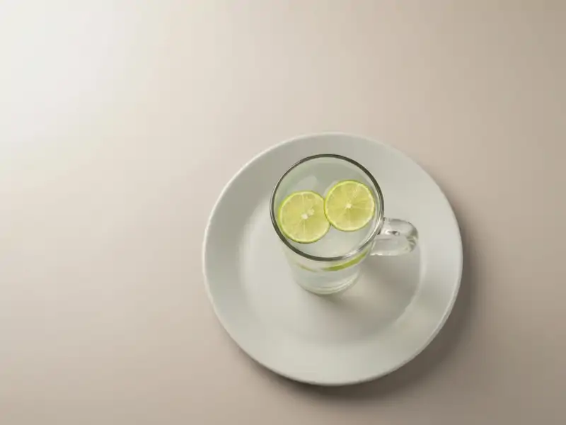 A single tall glass of coconut water with lime wedges